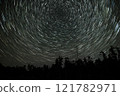 Star trails create mesmerizing patterns above a dark forest at night 121782971