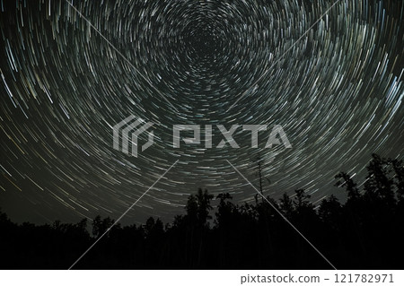 Star trails create mesmerizing patterns above a dark forest at night Star trails create mesmerizing patterns above a dark forest at night 121782971
