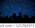 Stars create beautiful streaks in the night sky above a forest landscape during a clear evening 121782973