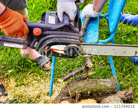 A man cuts down a tree with an electric saw. Sawdust flies in all directions from the chainsaw. Cutting wood with a chain saw 121784018