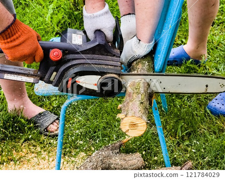 A man cuts down a tree with an electric saw. Sawdust flies in all directions from the chainsaw. Cutting wood with a chain saw 121784029