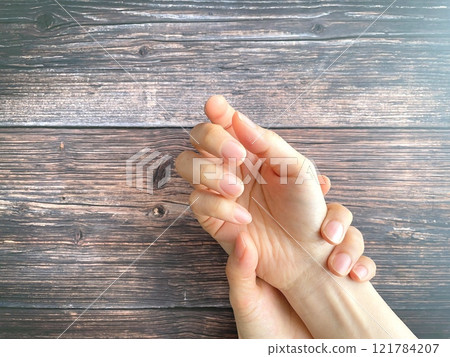 A woman's hand holding her right wrist on a desk 121784207
