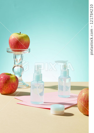 On a light blue backdrop An apple is positioned next to a mockup of blue beauty products on pink paper, placed on a yellow surface. Cosmetics advertising photo. On a light blue backdrop An apple is positioned next to a mockup of blue beauty products on pink paper, placed on a yellow surface. Cosmetics advertising photo. 121784210