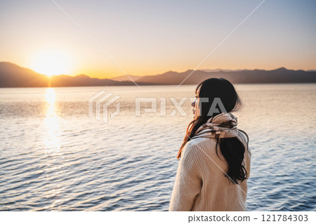 Evening lake and a young woman in a knitted sweater and scarf 121784303