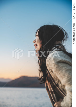 Evening lake and a young woman in a knitted sweater and scarf 121784326