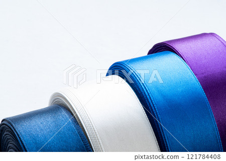 Colorful Rolls of Satin Ribbon in White, Blue, and Purple on a Light Background for Crafting and Decoration Colorful Rolls of Satin Ribbon in White, Blue, and Purple on a Light Background for Crafting and Decoration 121784408