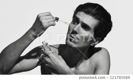 Man with smooth skin, applying serum with dropper against white background in black-and-white filter. Cosmetic, skin care product. Man with smooth skin, applying serum with dropper against white background in black-and-white filter. Cosmetic, skin care product. 121785089
