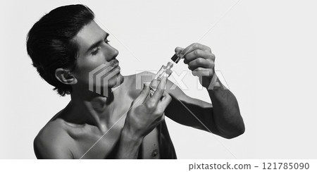 Photo of shirtless man with focused expression, examining serum bottle, lifting dropper against white background. Skin care products. Photo of shirtless man with focused expression, examining serum bottle, lifting dropper against white background. Skin care products. 121785090