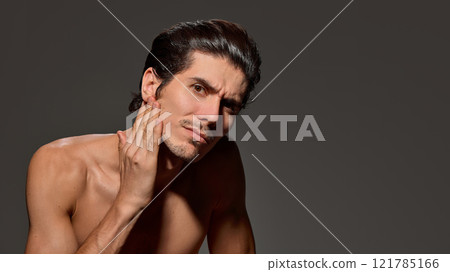 Man looking upward slightly, shows soft smile against dark background. His posture and sleek hairstyle suggest ease and confidence. 121785166