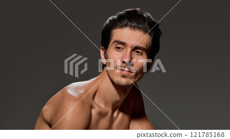Handsome, shirtless man holds his face with one hand, his eyebrows furrowed in thoughtful expression against deep dark background. 121785168