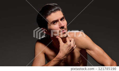 Handsome, stylish man resting his chin on his hand, creating inquisitive pose, highlights his focused expression against dark background. 121785190