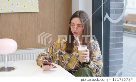 Pretty brunette with phone in hands relaxing in cafe. Woman drinking coffee cocktail 121785784
