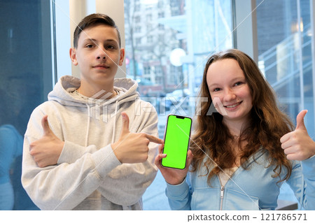 Group of cheerful students taking a selfie with a cellphone while sitting outdoors with a laptop, capturing a fun moment together, showcasing friendship, technology, and student life on campus. High 121786571