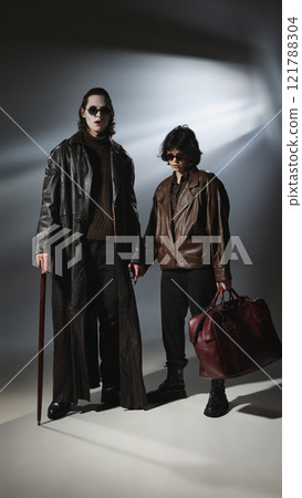Vampire and female companion stand together, wearing stylish dark coats. Companion holds leather bag. 121788304