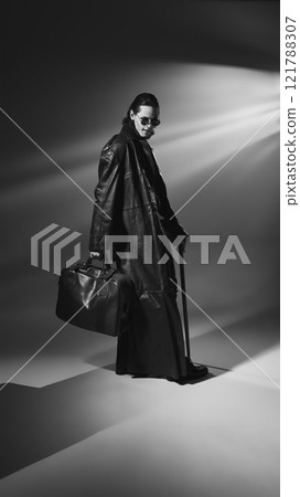 Monochrome, full length portrait of vampire wearing round glasses and leather coat poses holding bag and cane. Lord of darkness. 121788307