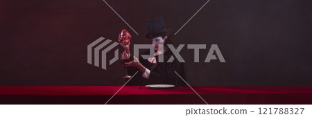 Banner. Vampire sitting at red table and having dinner, draining blood from heart into wine glass on dark vintage background with copy space. 121788327