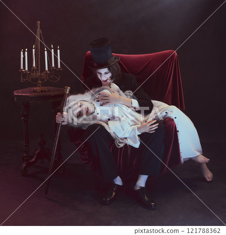 Man in black suit, vampire, holds woman dressed in white on his lap, gazing intently, next to vintage candelabra. 121788362