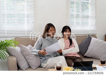Female higher education student using laptop and studying book in home, Online learning. 121788606