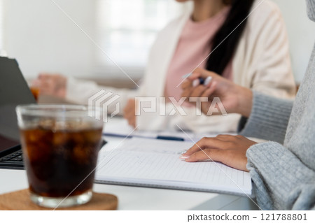 Female higher education student using laptop and studying book in home, Online learning. Female higher education student using laptop and studying book in home, Online learning. 121788801