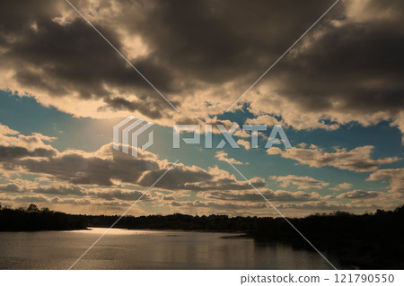 Gloomy evening sky landscape with thunderclouds and water surface of the river.the sun shining through clouds over a lake Gloomy evening sky landscape with thunderclouds and water surface of the river.the sun shining through clouds over a lake 121790550
