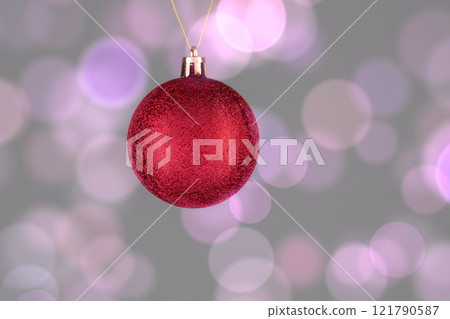 A red Christmas ball on a gray background with spots of pink bokeh. A red Christmas ball on a gray background with spots of pink bokeh. 121790587