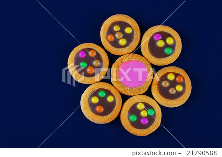 A creative sweet dessert. Cookies with chocolate filling and pink glaze on a dark blue background in the form of a flower. A creative sweet dessert. Cookies with chocolate filling and pink glaze on a dark blue background in the form of a flower. 121790588