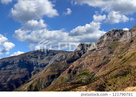 Majestic mountain against a cloudy blue sky background. Beautiful view of mountain outcrops with hill covered with green vegetation on popular landmark or hiking location in Cape Town, South Africa Majestic mountain against a cloudy blue sky background. Beautiful view of mountain outcrops with hill covered with green vegetation on popular landmark or hiking location in Cape Town, South Africa 121790781