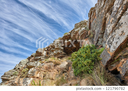 Copy space on a rocky mountain with plants and shrubs growing against a cloudy sky background. Rugged, remote and quiet landscape with boulders and stones on a cliff to explore during a scenic hike 121790782