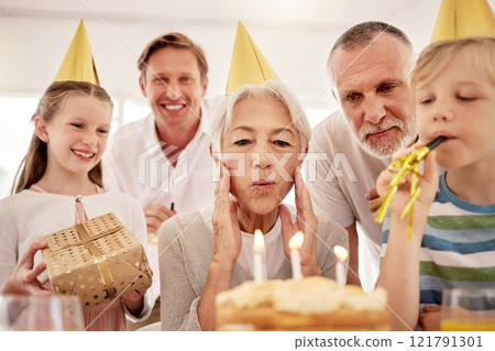 Senior woman celebrating a birthday with family at home, wearing party hats and blowing whistles. Grandma looking at birthday cake and being joyful while surrounded by her grandkids, husband and son 121791301
