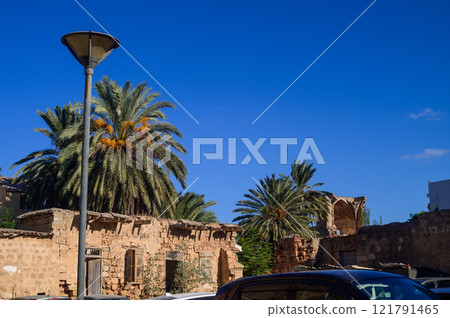 Old stone structures under a vibrant blue sky surrounded by lush palm trees during a sunny day 121791465