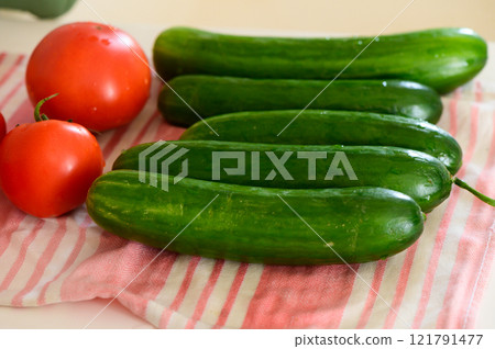 Fresh cucumbers and ripe tomatoes arranged on a striped kitchen towel in morning light Fresh cucumbers and ripe tomatoes arranged on a striped kitchen towel in morning light 121791477