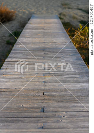 A tranquil wooden walkway leading into nature at sunset by the riverside invites peaceful contemplation. 121791497