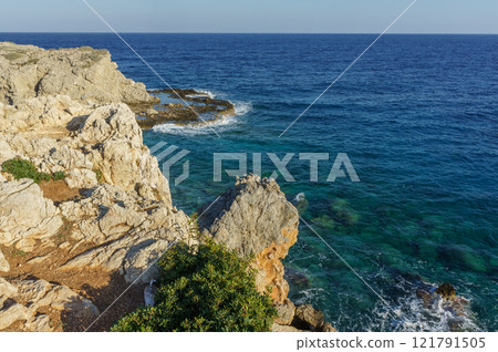Serene coastal view from rocky cliffs overlooking the clear blue sea during a bright sunny day. 121791505