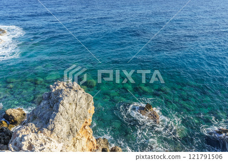 Vivid blue waters gently lapping against rocky shores at a tranquil seaside escape. Vivid blue waters gently lapping against rocky shores at a tranquil seaside escape. 121791506