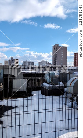 隆冬陽光明媚的日子，空調設備穿過覆蓋著雪的屋頂的圍欄 121791549