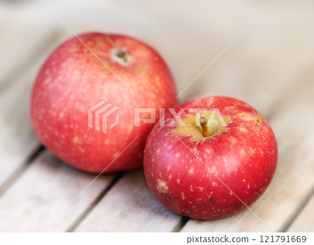 Two red apples on a wooden table indoors. Eat healthy and watch your diet. Fruit contains essential vitamins to boost your immunity. Closeup of a delicious snack vegans and vegetarians can enjoy 121791669