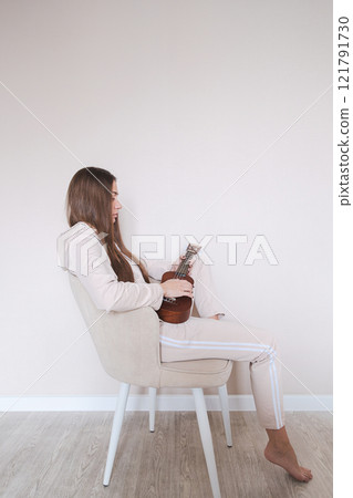 Woman with ukulele sitting on a chair. 121791730