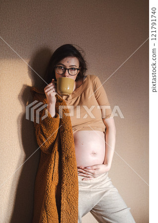 Pregnant woman holding her belly and drinking tea from mug. Pregnant woman holding her belly and drinking tea from mug. 121791740