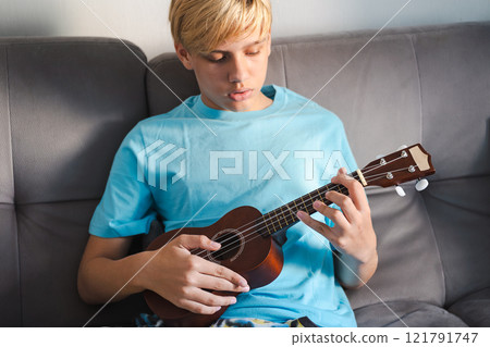 Teen boy exercising playing ukulele, at home. 121791747