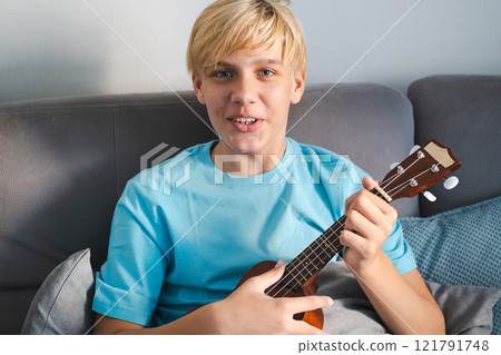 Laughing teenager playing ukulele, at home. 121791748