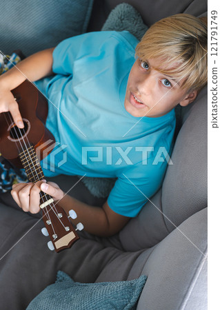Laughing teenager playing ukulele, at home. Laughing teenager playing ukulele, at home. 121791749