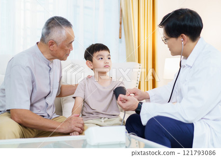Grandfather taking his sick grandson to see a doctor in hospital, then doctor is talking with them and using stethoscope to listen the boy heart beat. Doctor examines symptom in the boy. 121793086