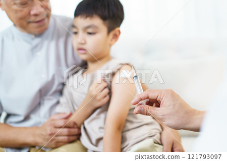 Asian little boy with grandfather in the doctor office in hospital is vaccinated by doctor. Doctor injecting a shot of vaccine on the boy's arm. Illness prevention concept. 121793097