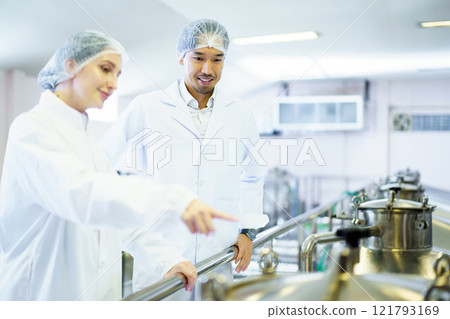 Team of quality control officers or factory engineers are inspecting inside the beverage manufacturing facility. Man and woman engineers working in a food production factory. Team of quality control officers or factory engineers are inspecting inside the beverage manufacturing facility. Man and woman engineers working in a food production factory. 121793169