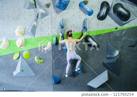 Asian sportswoman practices an indoor rock climbing wall. Asian sportswoman practices an indoor rock climbing wall. 121793254