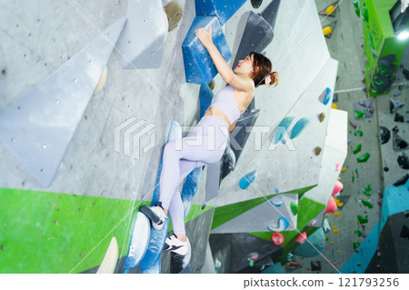 Asian sportswoman practices an indoor rock climbing wall. Asian sportswoman practices an indoor rock climbing wall. 121793256