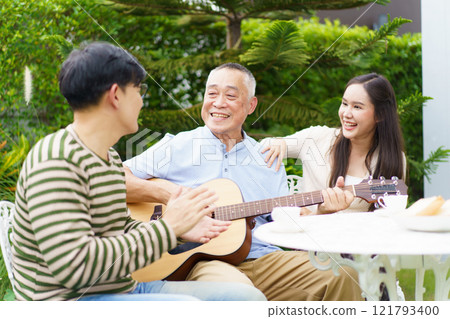 Happy multi-generation Asian family living together in weekend. Happy Asian family spending time together, man and woman let their father playing a guitar and singing in backyard garden at home.  121793400