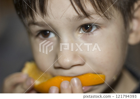 A little boy is eating a slice of orange, close-up. 121794393