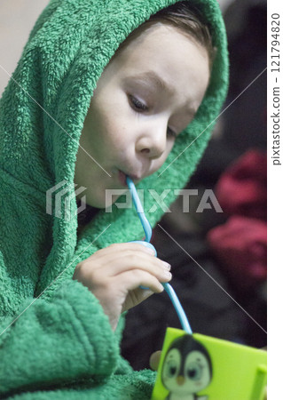 A little boy in a terry bathrobe holds a cup with a straw. 121794820
