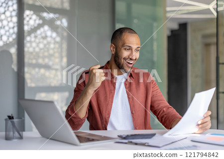 Successful financier celebrating victory and success reading report. Man behind paperwork working with laptop inside office with documents, businessman in shirt got winning investment results. 121794842